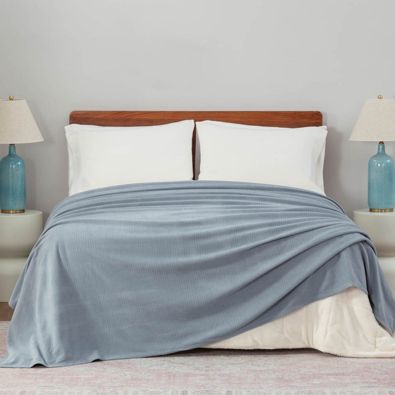 Polartec Softec Microfleece blanket in polar blue, draped elegantly over a white bed.