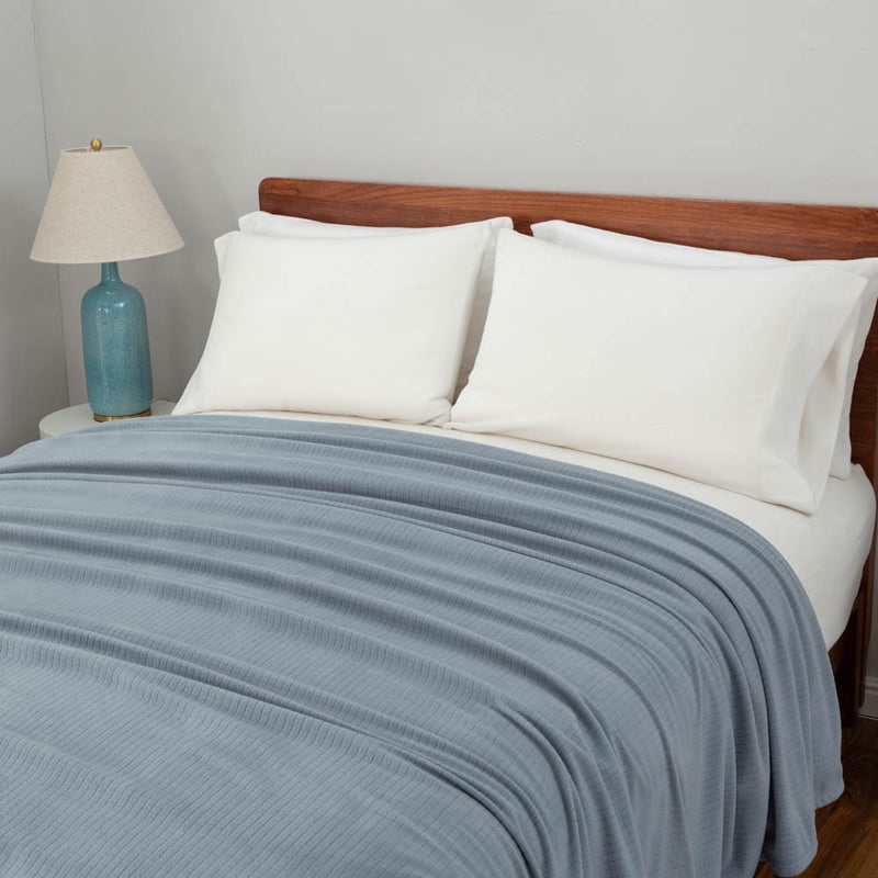 Polartec Softec Microfleece blanket in polar blue, draped elegantly over a bed.