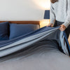 A woman pulling a Polartec Softec Microfleece blanket in polar blue elegantly over a bed.