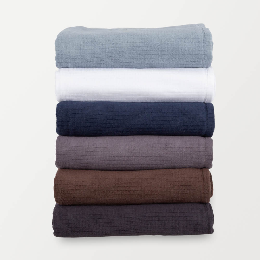 Stack of six folded Polartec Softec Microfleece blankets in various colors: light blue, white, navy, light grey, brown, and black.