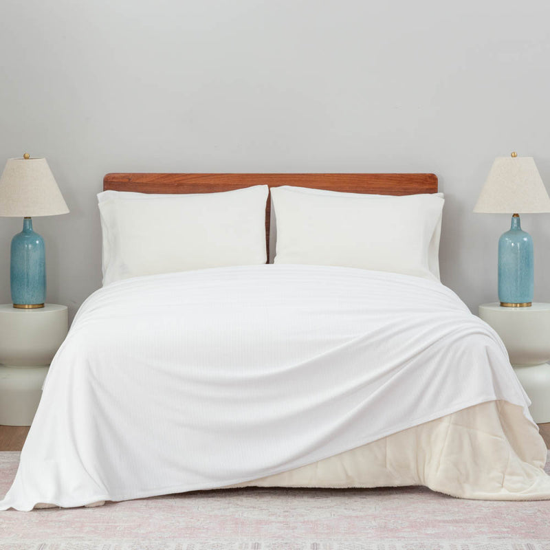 Bright bedroom scene with a Polartec Softec Microfleece blanket in white spread neatly over a bed.