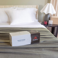 Box of Berkshire Polartec blankets on a bed with pillows and a lamp in the background