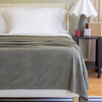 Gray blanket draped over a bed with a nightstand in the background