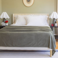 Bedroom with a bed covered in a green blanket, white pillows, and two nightstands with lamps.