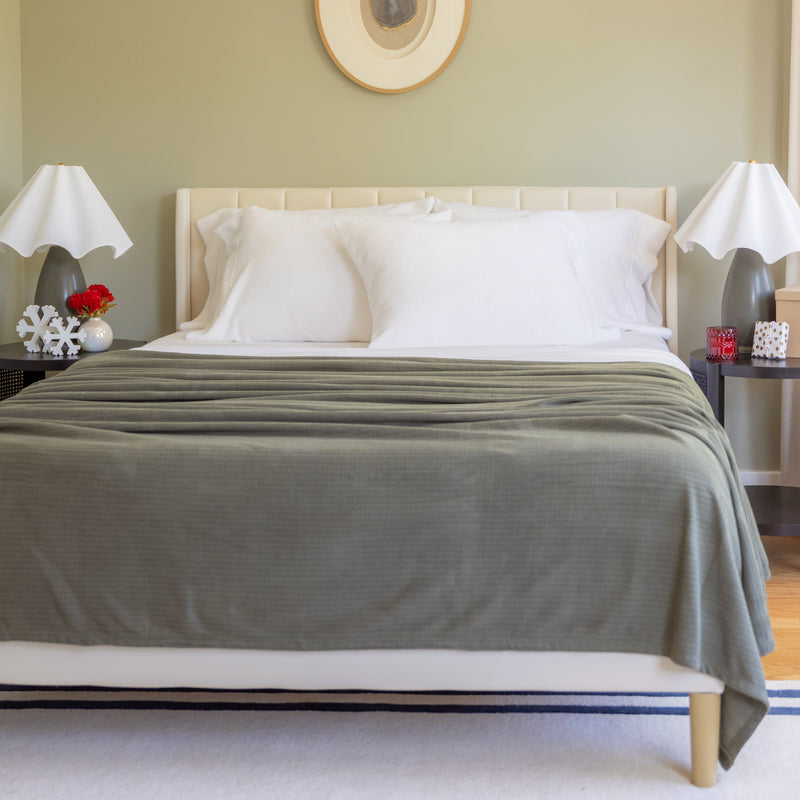 Bedroom with a bed covered in a green blanket, white pillows, and two nightstands with lamps.