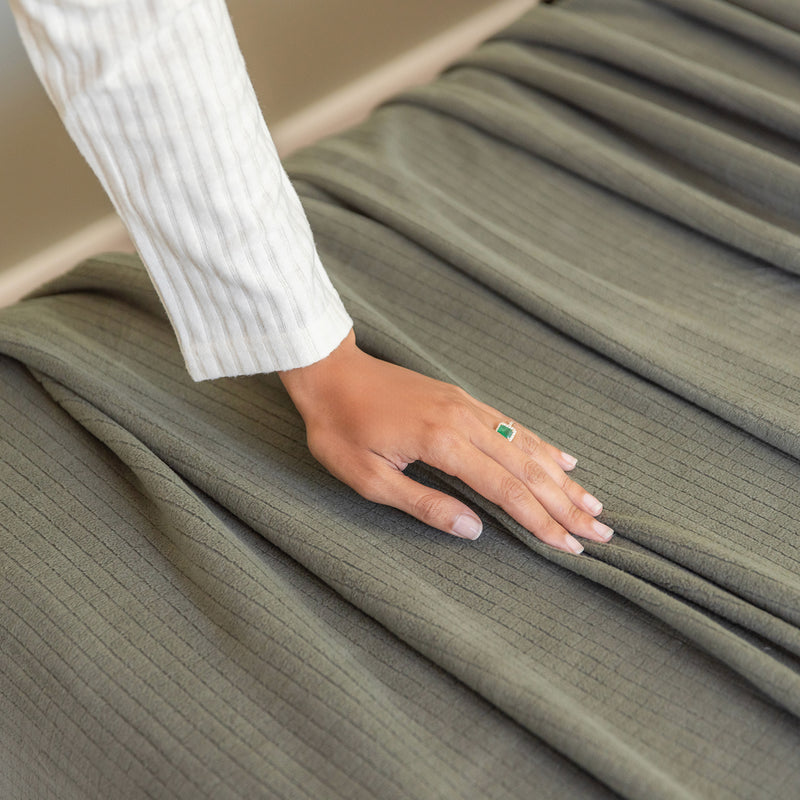 Person wearing a white shirt with a green gemstone ring touching olive green fabric.
