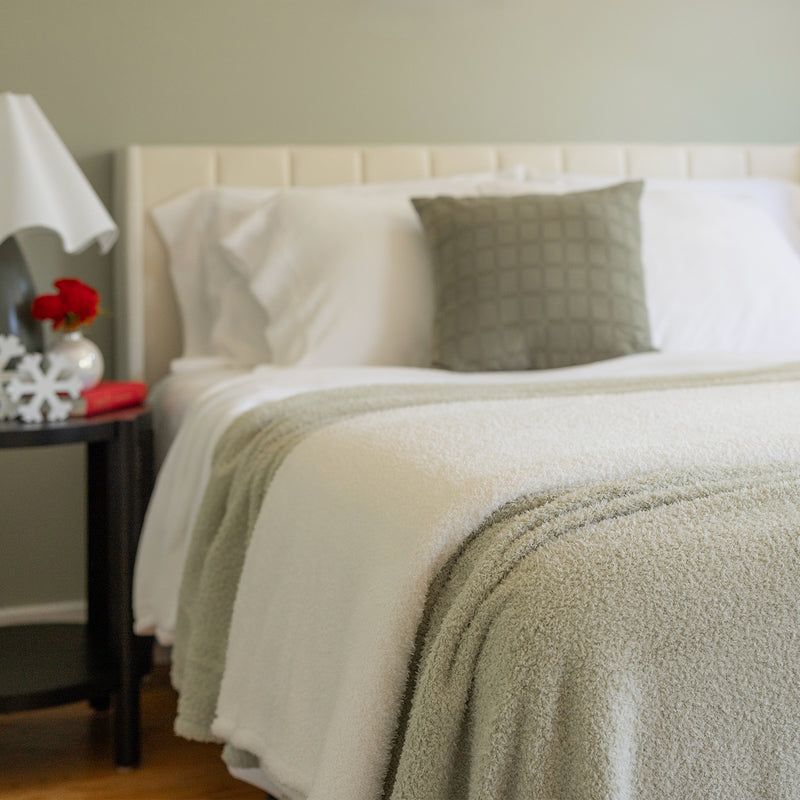 Neatly made bed with white bedding and a green throw blanket in a bedroom setting.