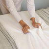 Person arranging white bedding on a bed