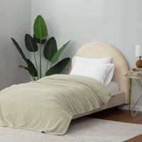 A neatly styled bed with a green Retro Comfort Plush Blanket in a minimalist bedroom featuring a houseplant.