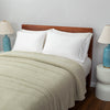 A bed covered with a light green Retro Comfort Plush Blanket, styled with white pillows and bedside lamps.