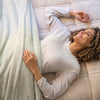 A person lying on a bed, wrapped in a green Retro Comfort Plush Blanket, smiling and relaxed.