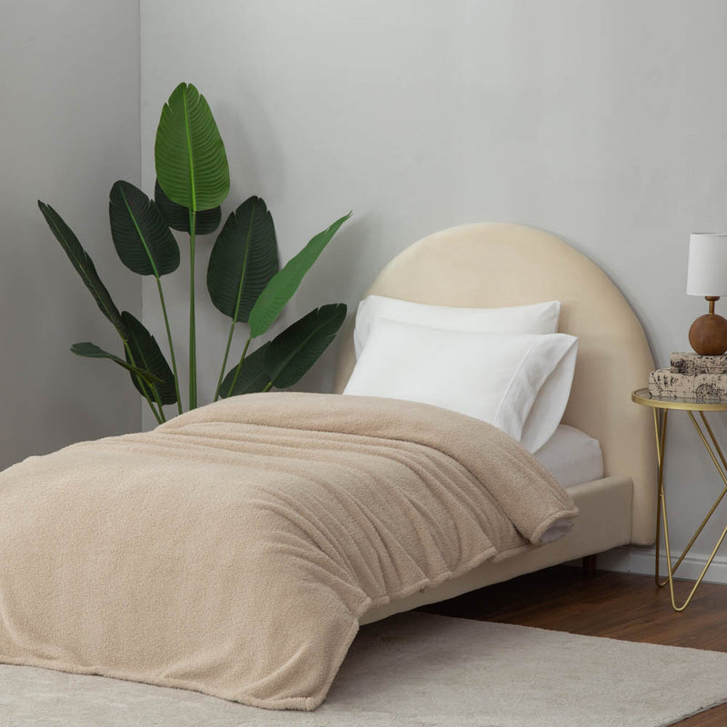 A neatly styled bed featuring a tan Retro Comfort Plush Blanket and minimalist décor with bedside lamps.