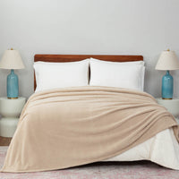 A bed styled with a tan Retro Comfort Plush Blanket, white pillows, and light blue bedside lamps.