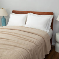 A neatly styled bed featuring a tan Retro Comfort Plush Blanket and a minimalist décor with bedside lamps.