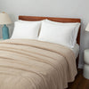 Beige blanket on a bed with white pillows and wooden headboard
