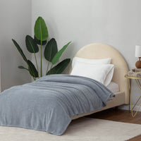 A minimalist bedroom with a blueRetro Comfort Plush Blanket on a bed, accompanied by a houseplant and simplistic furniture.