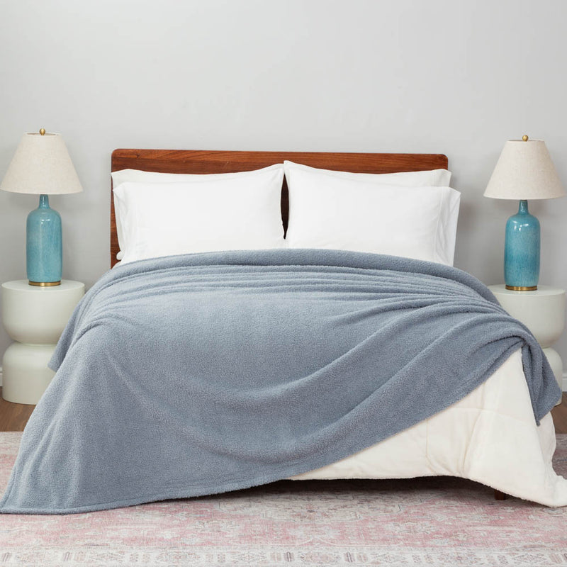 A bed covered with a blue Retro Comfort Plush Blanket, styled with white pillows and light blue bedside lamps.