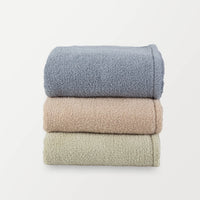 A stack of three Retro Comfort Plush Blankets in blue, beige, and green, neatly folded.