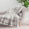 A plaid heated throw blanket draped over a chair next to a potted plant.