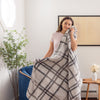 A person standing next to a chair wrapped in a plaid throw blanket, smiling.