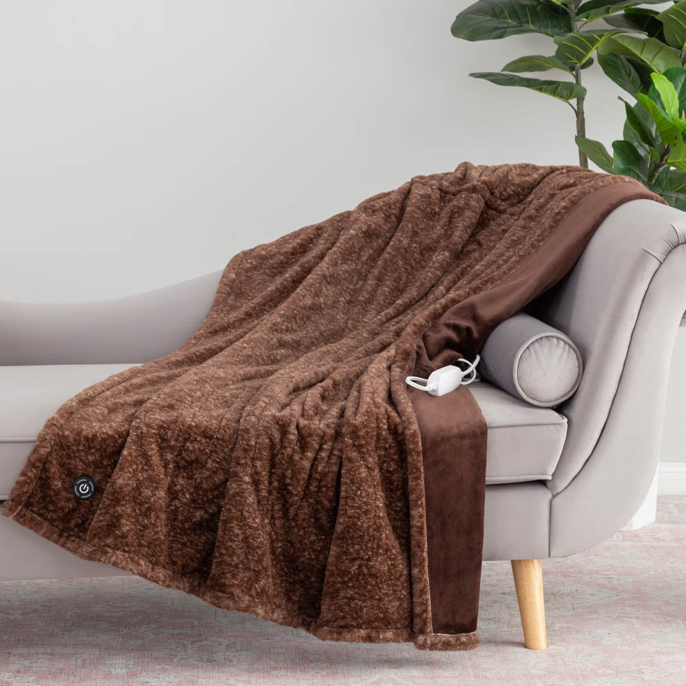 A brown heated throw with a power button on its surface draped over a grey chair with a plant in the back.