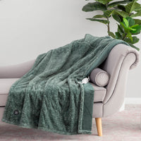 A dark green heated throw draped over a grey chair, with a plant in the background.