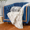 A blue couch draped with a white and gray patterned throw blanket and matching pillows.