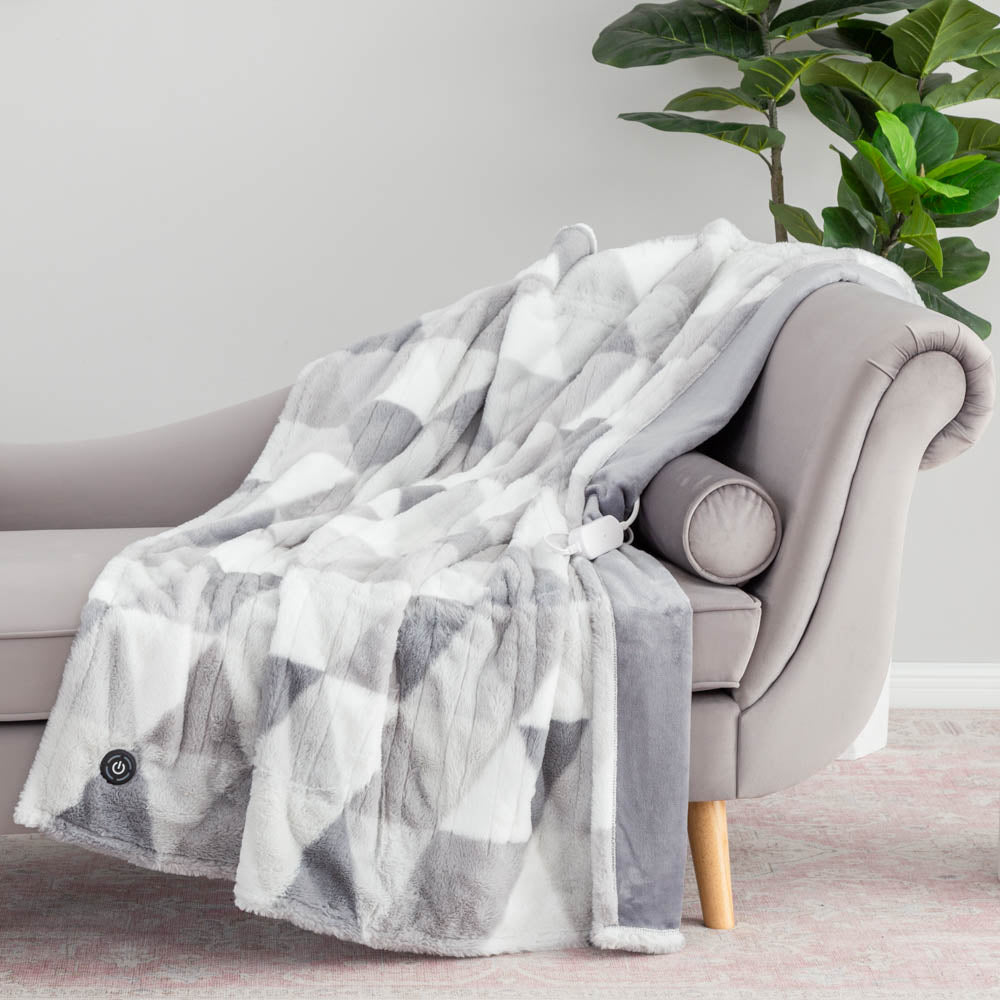 A grey patterned diamond heated throw draped over a grey chair with a plant in the background. 