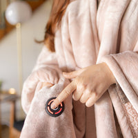 Close-up of the power button on the pink heated throw with a woman pressing it.