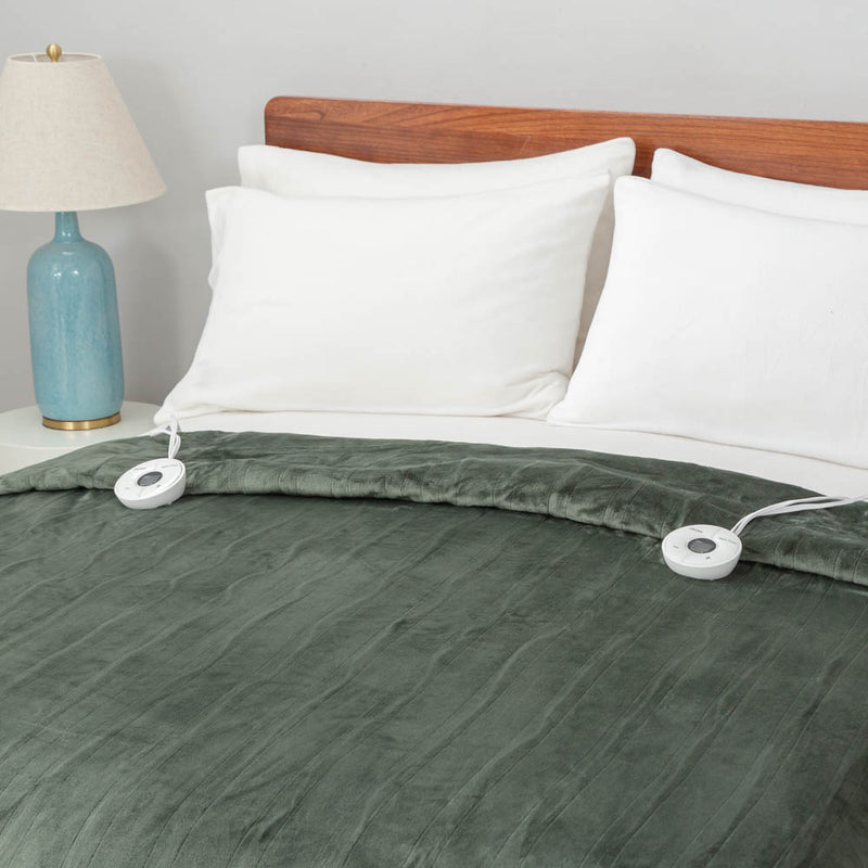 A neatly made bed with a green heated blanket, white pillows, and a bedside lamp.