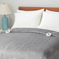 A neatly made bed with a gray heated blanket, white pillows, and a bedside lamp.