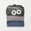 A stack of three folded heated blankets in green, gray, and blue, with two round controllers resting on top.