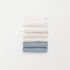 A stack of 6 pillowcases in white, cream, and blue folded neatly on a white surface.