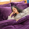 A woman laying in a bed dressed in purple velvety sheets and comforter.