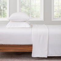 White bedding set on a wooden bed with large windows in the background
