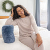 Woman sitting on a bed with a blue pillow, wearing a beige ribbed loungewear set.
