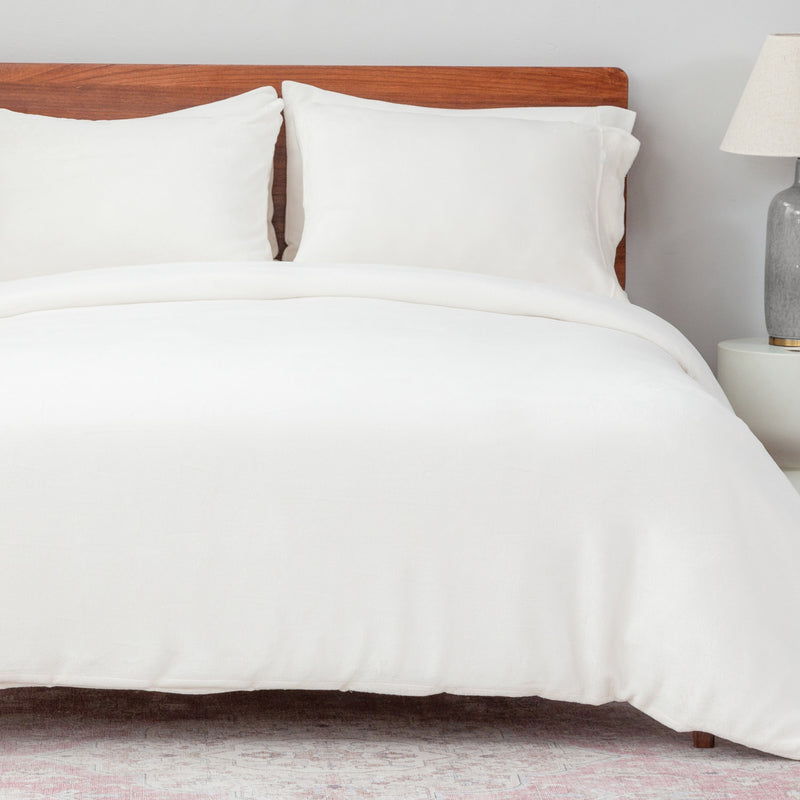 Bed with white bedding and wooden headboard against a light gray wall.