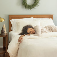 Woman sleeping in a bed with white bedding and wooden headboard, room decorated for Christmas.