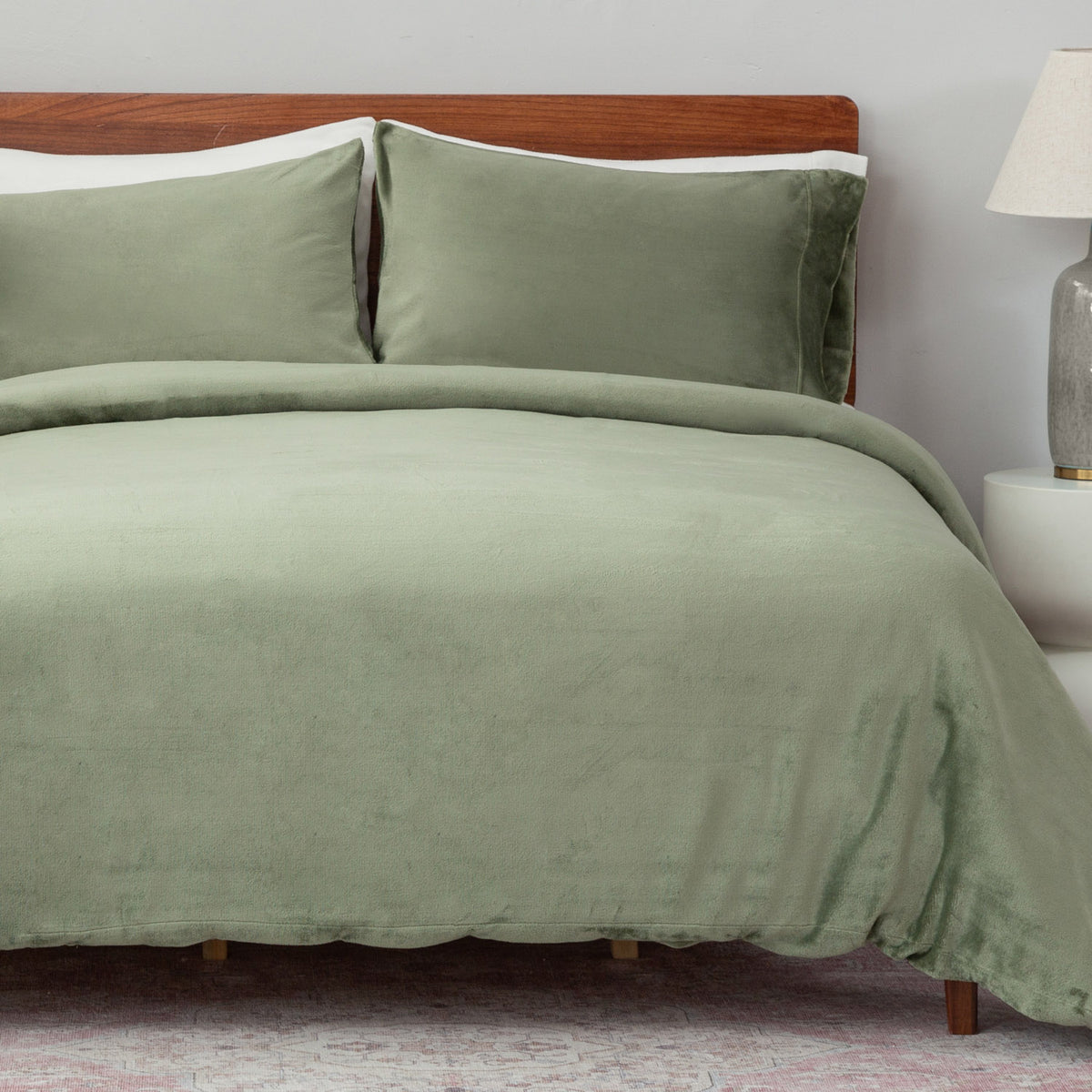 Green bedding set on a bed with a wooden headboard and lamp in the background.