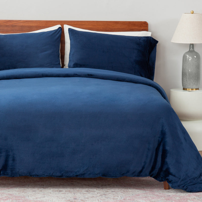 Navy blue bedding set on a bed with a wooden headboard and lamp in the background.