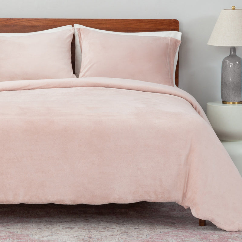 Bed with pink bedding and wooden headboard in a room setting.