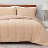 Beige textured comforter on a bed with pillows and a lamp in the background.