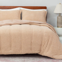 Beige textured comforter on a bed with pillows and a lamp in the background.