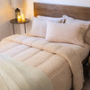 A neatly made bed featuring a tan sherpa comforter set, with white pillows and a warm bedside ambiance