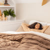 Woman lying in bed under a brown comforter in a cozy bedroom.