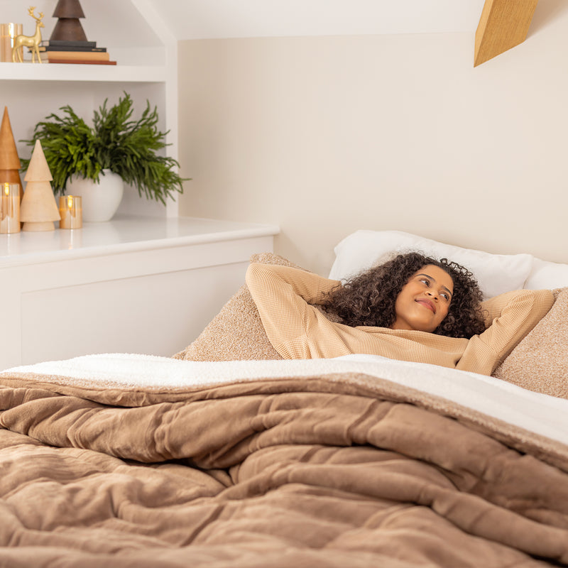 Woman lying in bed under a brown comforter in a cozy bedroom.