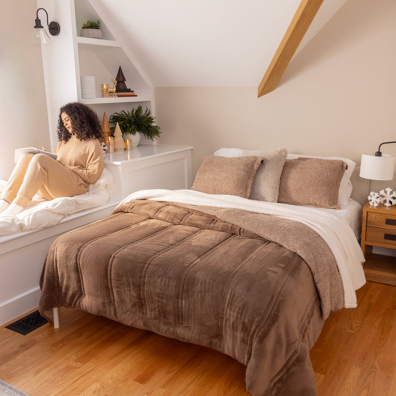 Woman reading a book on a bed with brown bedding in a cozy bedroom.
