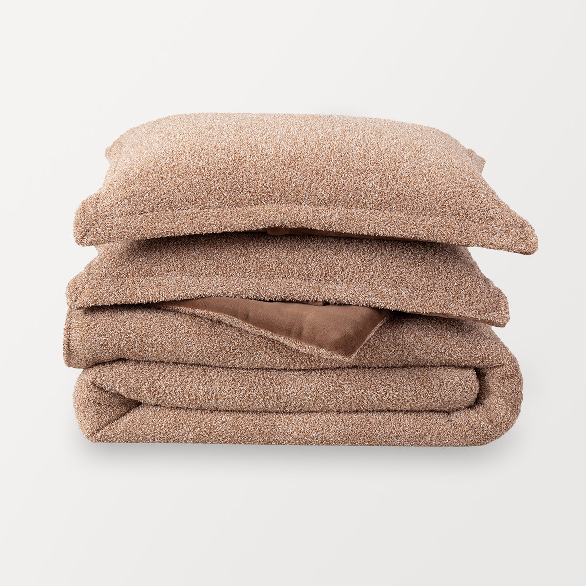 A single retro plush comforter folded and stacked with two matching pillow shams stacked in a pile. Sumatra Blend color is a medium brown color mixed with white specs.  