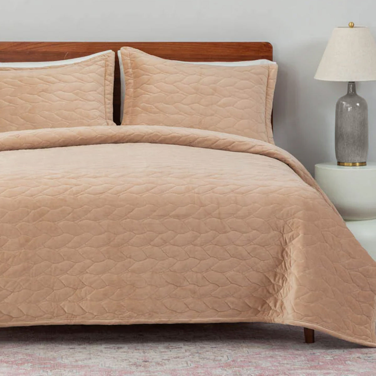 Beige quilted bedding set on a bed with a wooden headboard and lamp in the background.