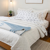 Bed with white comforter, blue blanket, and patterned pillow in a bedroom setting.